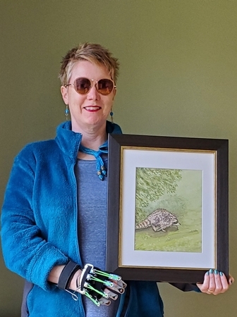 Sandra with one of her framed watercolours, a running raccoon